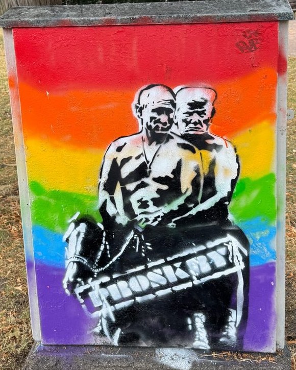 Pochoir Be pride : deux hommes torse nu à cheval sur fond arc-en-ciel, barrés du tampon Proskry, peints sur un coffret de rue