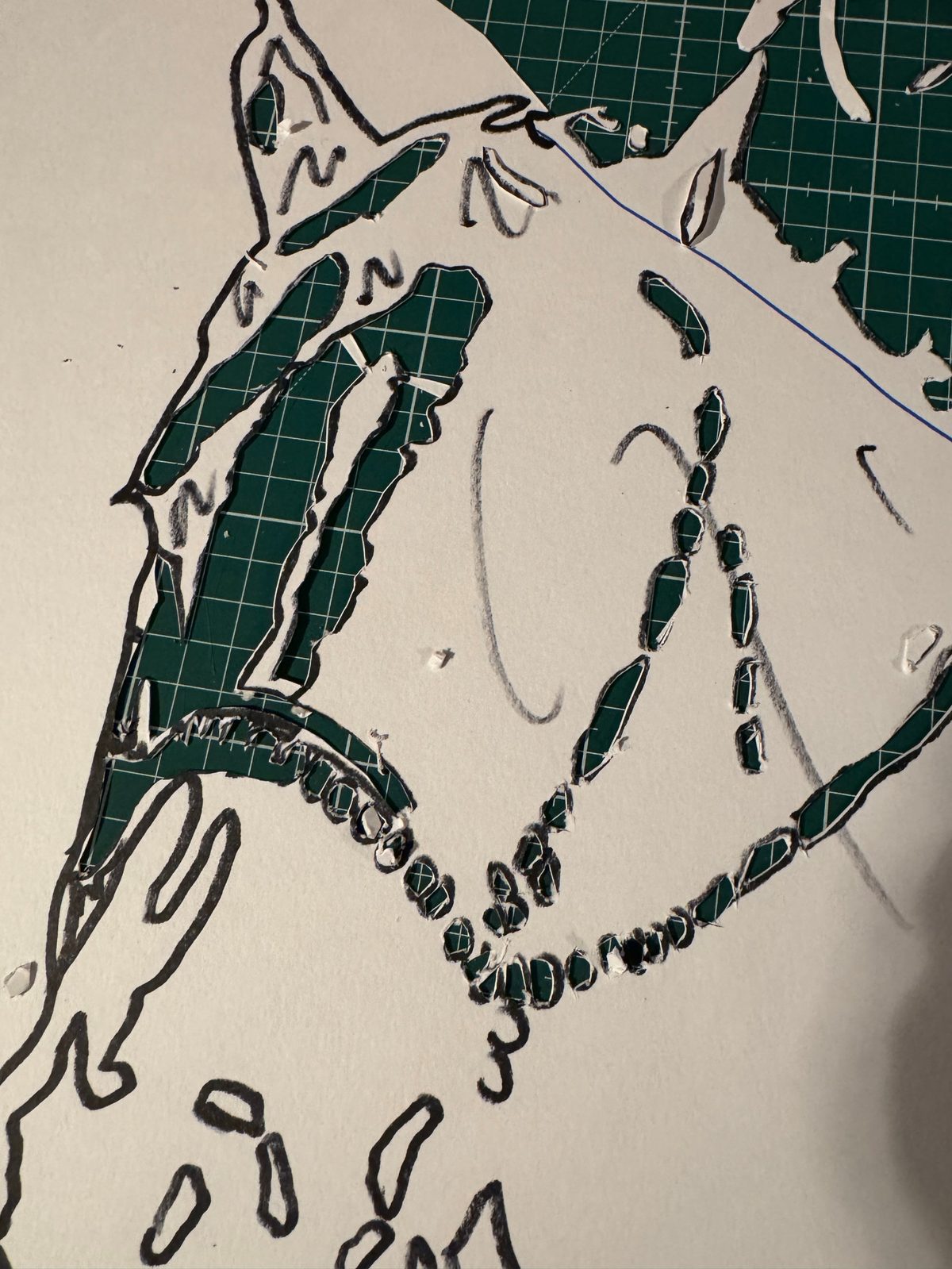 Détail de la découpe du pochoir au cutter : les traits noirs tracés sur le papier et les parties évidées laissant voir le tapis de coupe vert