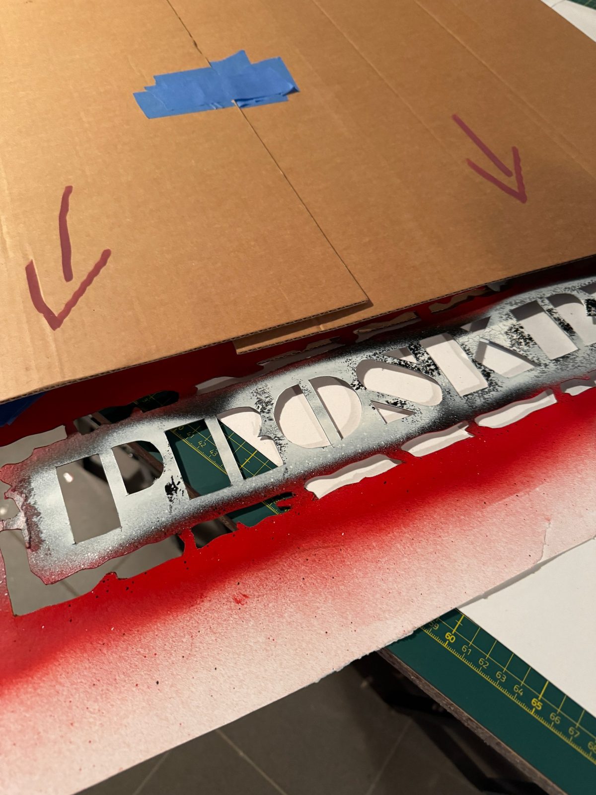 Le pochoir du tampon Proskry à l'atelier, les lettres découpées et la bombe rouge appliquée