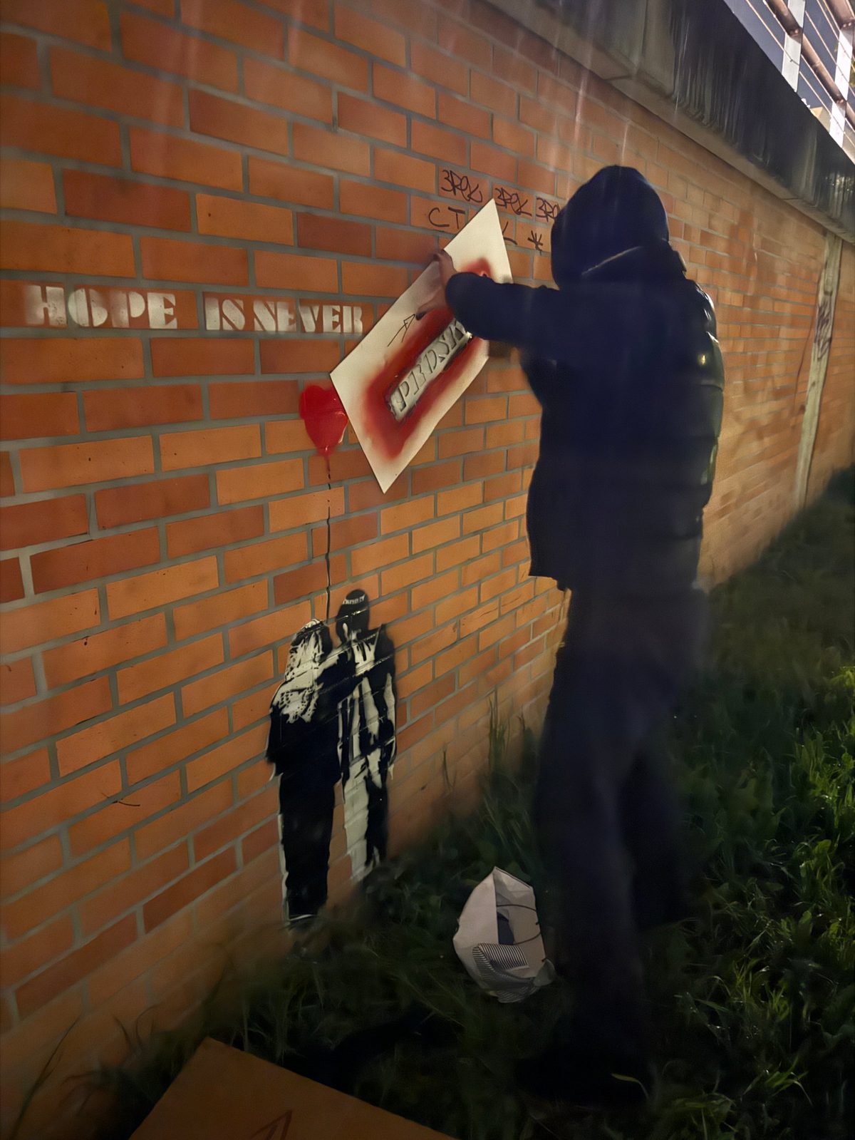 La pose de nuit : le pochoir du tampon plaqué contre le mur de briques et peint à la bombe